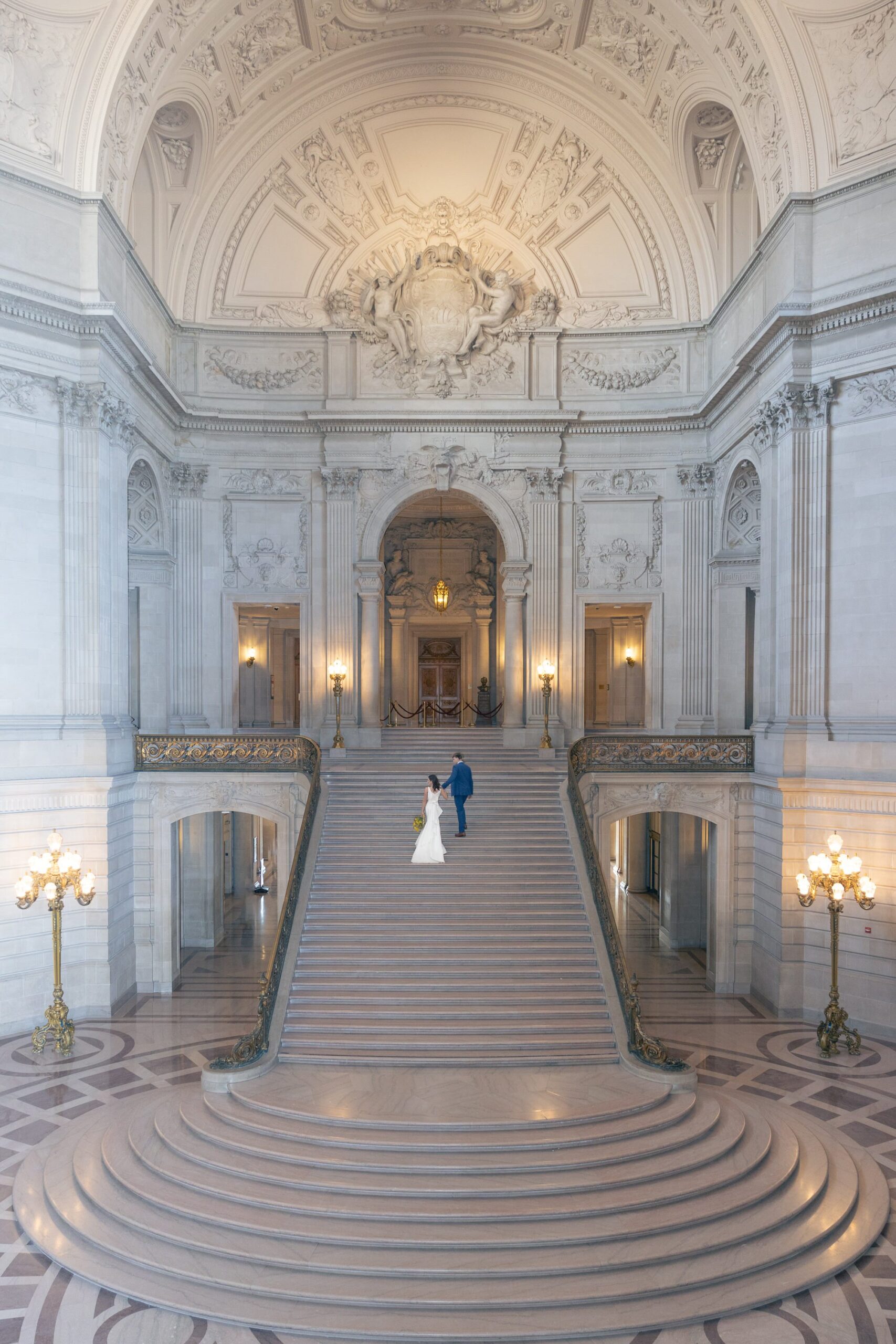 Bride and groom walking up the grand staircase inside San Francisco City Hall venue